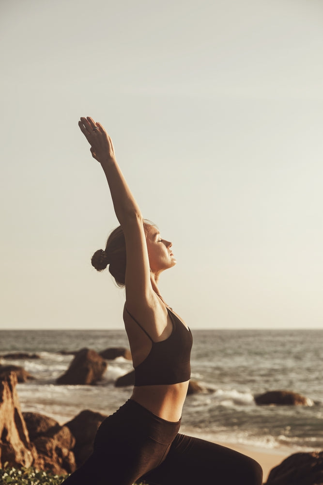 Woman performing a pilates stretch by the ocean view on the beach